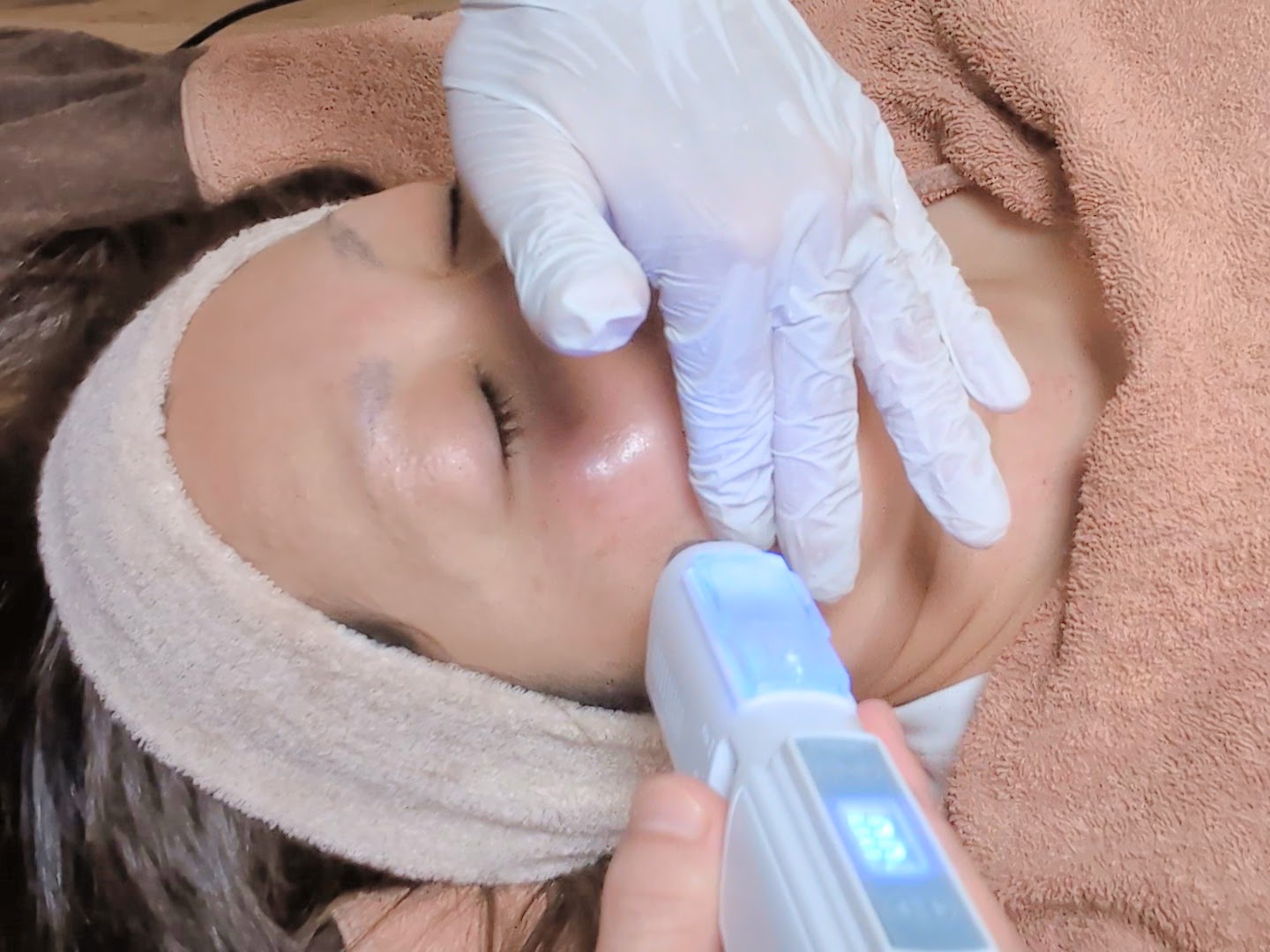 Aesthetician performing facial treatment with handheld device on relaxed client's face